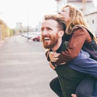 Couple of young beautiful redhead and blonde millennial woman and man, she is riding piggy back, both laughing - love, relationship, laughing concept