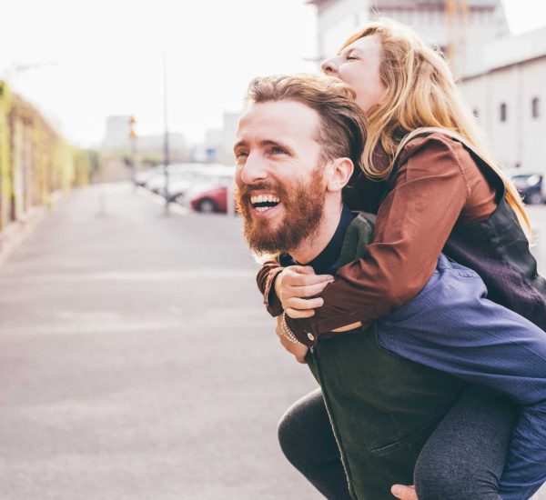 Couple of young beautiful redhead and blonde millennial woman and man, she is riding piggy back, both laughing - love, relationship, laughing concept
